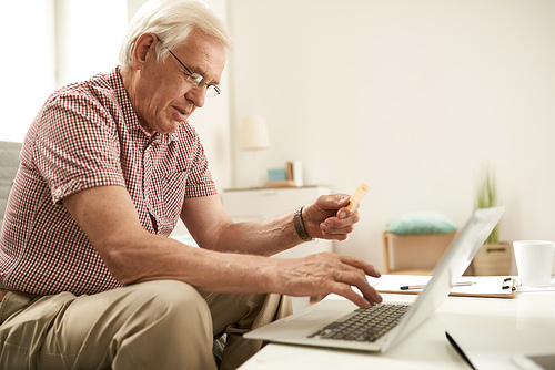 Side view portrait of senior man online shopping via laptop inputting credit card details for payment
