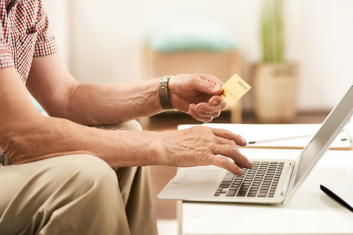 Closeup of senior man online shopping via laptop inputing credit card details for payment