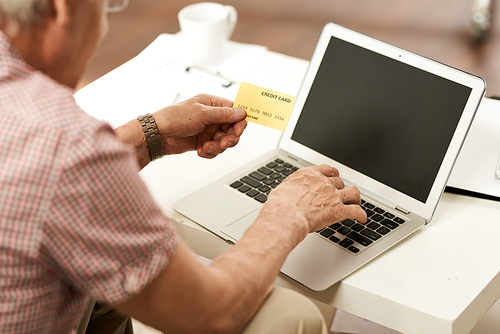 Portrait of senior man using credit card for internet purchase via laptop from home