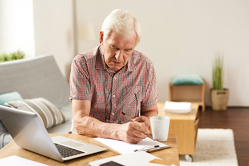 Portrait of senior man working with laptop at home counting finances