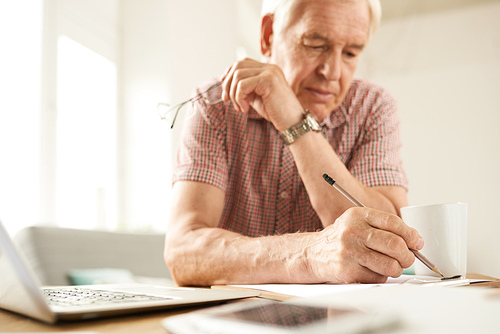 Portrait of modern senior man working at home and filling in papers