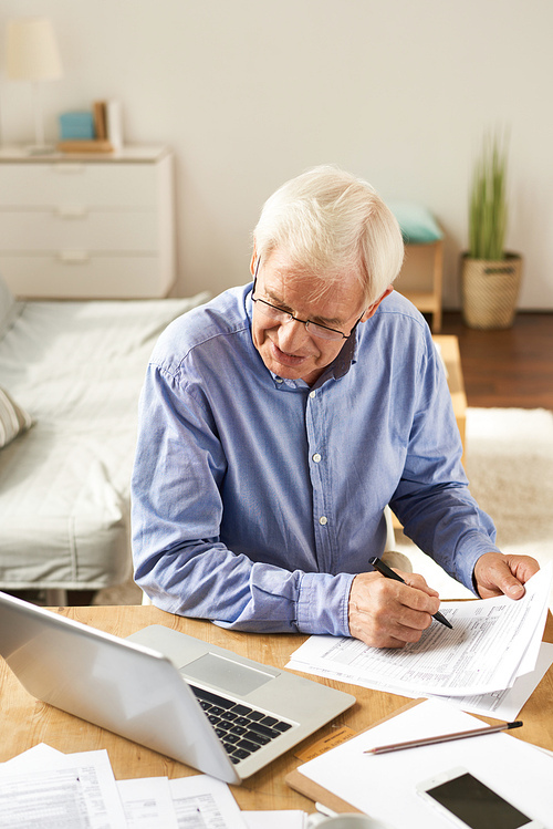 Portrait of modern senior man filling in application while working with laptop at home in cozy living room