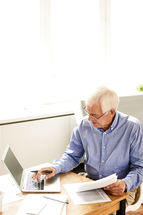 High angle portrait of modern senior man filling in application while working with laptop at home