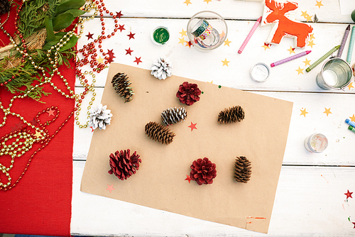 Making Christmas decorations: directly above view of wax crayons, handmade toy, Christmas wreath and colorful fir cones lying on wooden desk