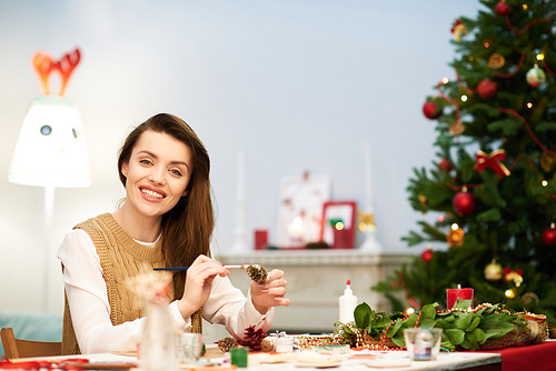 Waist-up portrait of attractive woman  with toothy smile while distracted from making Christmas decoration, interior of cozy living room on background