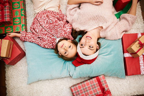 Directly above view of attractive young woman and her her cute little daughter enjoying each others company while lying on cozy carpet, Christmas gift boxes scattered around them