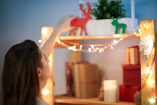 Back view of young woman decorating bookshelf with wooden deer figure while preparing for Christmas celebration