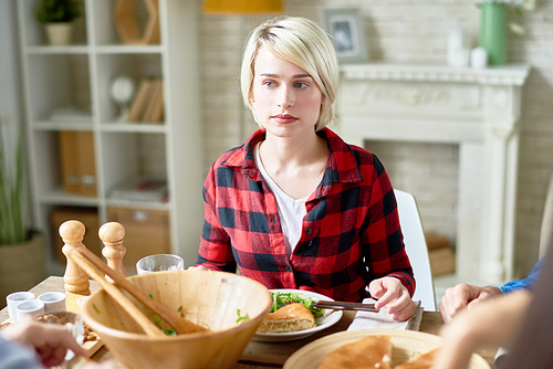 Portrait of blonde young woman sitting at festive dinner table with friends celebrating Thanksgiving