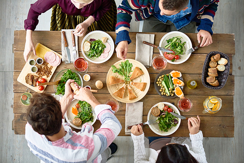 Above view of four people eating delicious food at festive dinner table in cafe celebrating holidays