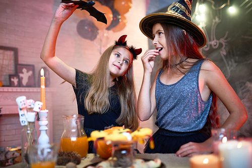 Portrait of two teenage girls wearing Halloween costumes playing with toy bat in decorated room during party