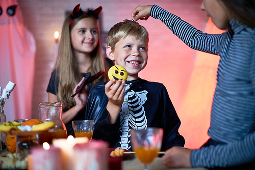 Portrait of children wearing Halloween costumes playing in decorated room during party, girl putting toy spider on top of cute little boys head