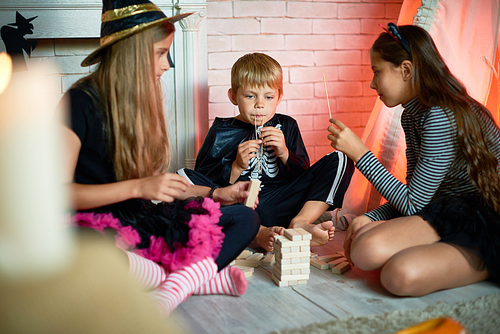 Portrait of three children wearing Halloween costumes, one boy and two girls, playing tower game in decorated studio