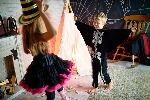 Portrait of two kids wearing Halloween costumes having fun playing in decorated studio