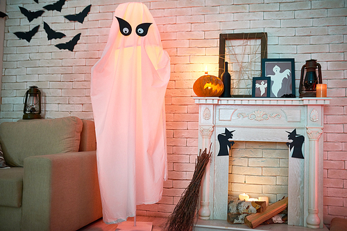 Common living room with sofa and fireplace decorated with Halloween toys and crafts such as lanterns, frames with ghosts, paper bats and withes, big ghost from fabric and broom