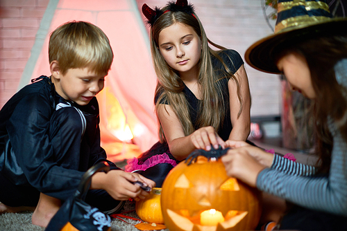 Curious concentrated friends sitting on floor and enjoying game with Halloween toys such as jack-o-lantern and spiders telling scary stories to each other