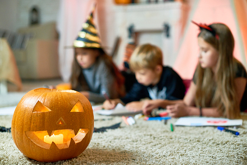 Focus on creative craved Halloween lantern with candle on shag carpet, kids drawing in background
