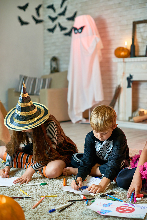 Portrait of three children wearing Halloween costumes drawing sitting on floor in decorated studio