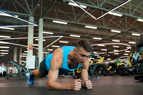 Full length portrait of handsome young man doing plank exercise while working out on floor in modern gym, copy space