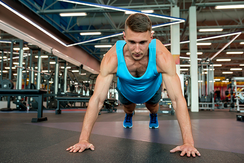 Front view portrait of handsome young man doing plank exercise while working out on floor in modern gym, copy space