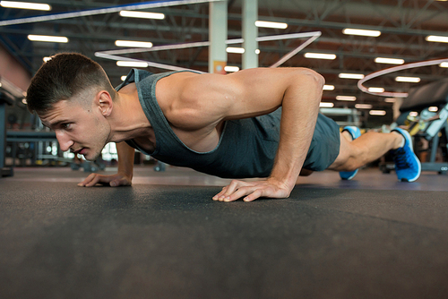 Full length portrait of handsome young man doing push-up exercise while working out on floor in modern gym