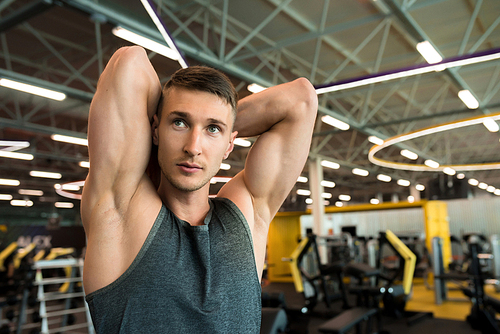 Portrait of handsome young man flexing arm muscles posing looking away while working out in modern gym, copy space