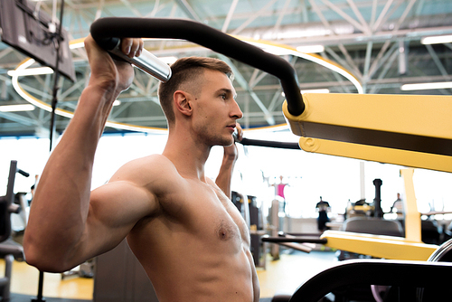 Side view portrait of handsome muscular man with no shirt training using exercise machine in modern gym, copy space