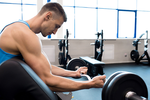 Side view  portrait of strong young man doing weightlifting exercises with heavy barbell  workout in modern gym, copy space