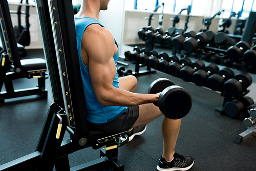 Side view portrait of handsome young man lifting dumbbells pumping arm muscles during strength training in modern gym