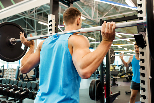 Back view portrait of strong man pumping arm muscles doing exercises with heavy barbell during workout in modern gym