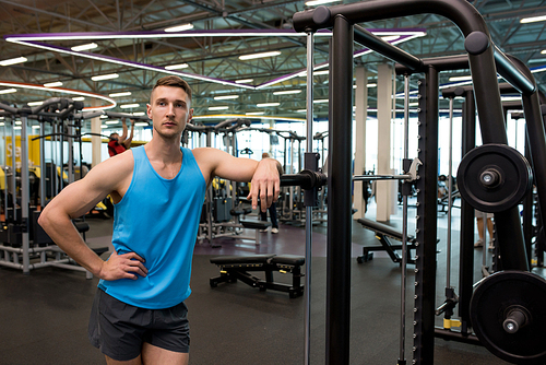 Portrait of muscular fitness trainer standing leaning on machines in modern gym , copy space