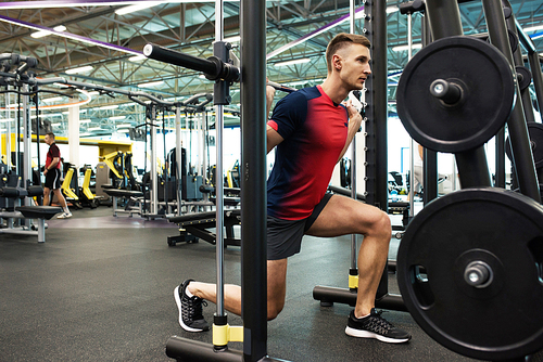 Portrait of strong young man doing weightlifting exercises with barbell at stand during workout in modern gym, copy space