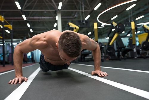 Portrait of young muscular man doing pushups on floor during workout in modern gym