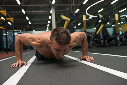 Front view portrait of shirtless muscular man pushing up from floor on modern gym during strength training