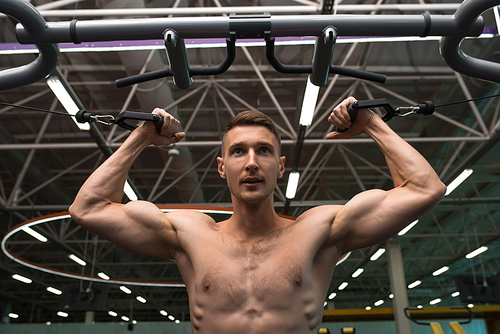 Low angle portrait of motivated young man with bare chest working out in modern gym using machines