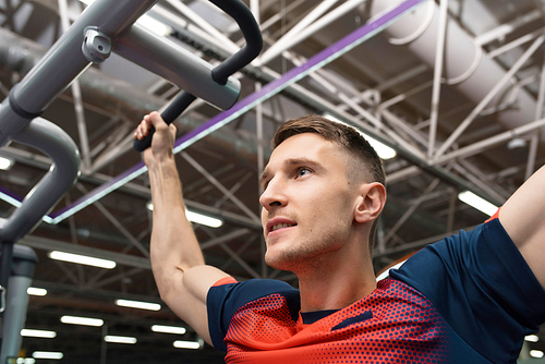 Low angle portrait of strong handsome  man using exercise machines during workout in modern gym