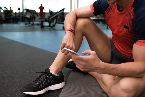 Mid section portrait of unrecognizable sportsman resting sitting on floor and using smartphone, typing text messages