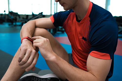 Mid-section portrait of unrecognizable modern sportsman checking fitness activity tracker sitting on floor in gym