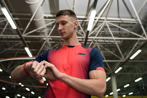 Low section portrait of handsome sportsman checking fitness tracker on wrist, setting device