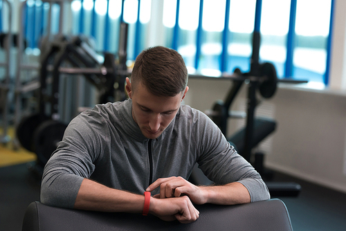 Portrait of handsome young man setting up fitness bracelet and checking data after workout in modern gym