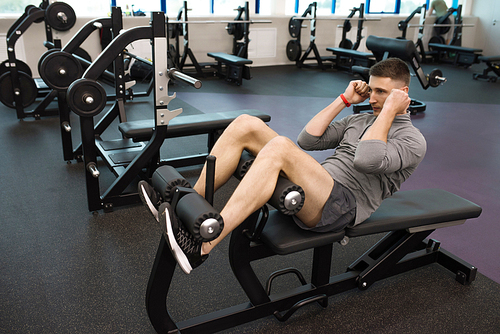 Portrait of strong young man doing crunches on stand during work out in modern gym