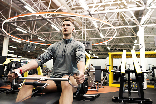 Portrait of handsome young man doing exercises using machines in modern gym in bright electric  light, copy space