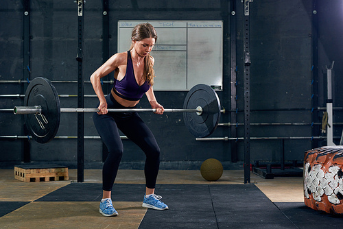 Portrait of strong young woman lifting  barbell during  workout in modern gym