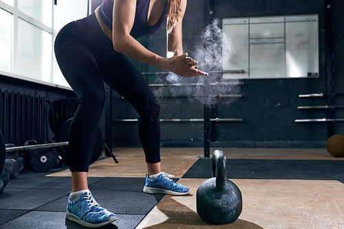 Low section  of unrecognizable young woman rubbing her hands with talk puffing cloud preparing to lift kettlebells during crossfit workout in modern gym