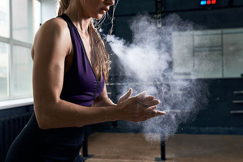Side view closeup of young  woman covering hands with talk in dark gym preparing for heavy weightlifting