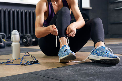 Closeup of young woman fixing her shoes taking break during workout in modern gym