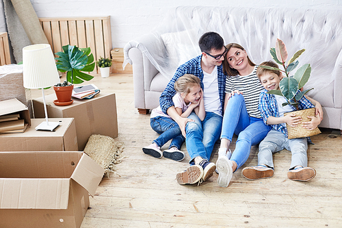 Full length portrait of loving young family gathered together in living room of new apartment and sharing ideas concerning interior design, cute little boy holding houseplant in hands