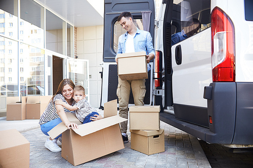 Portrait of loving young family with little child loading cardboard boxes into moving van outdoors