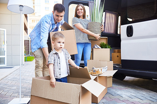 Portrait of happy young family with little son loading cardboard boxes into moving van outdoors