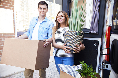 Portrait of happy young couple moving in new home, holding house plant and smiling  outdoors