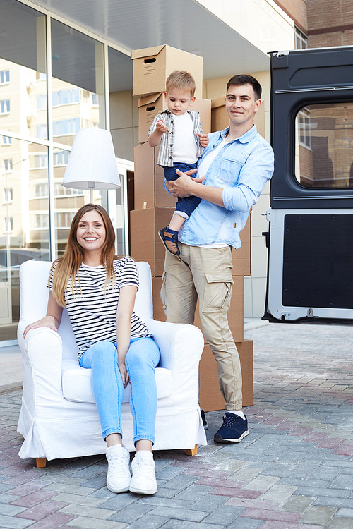 Portrait of happy young family sitting on armchair outdoors moving in new house, and posing for camera